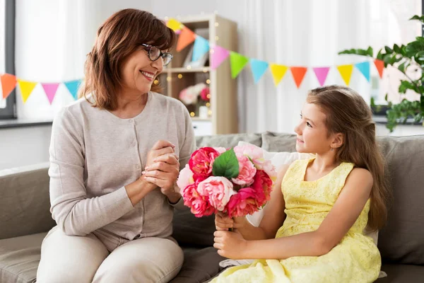 Neta dando flores avó em casa — Fotografia de Stock