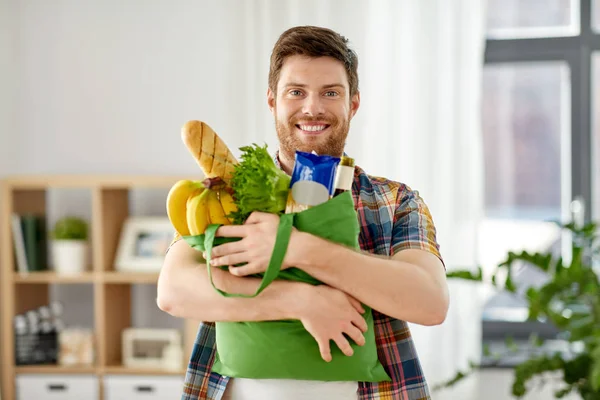 Uśmiechnięty młody człowiek z jedzeniem w torebce w domu — Zdjęcie stockowe