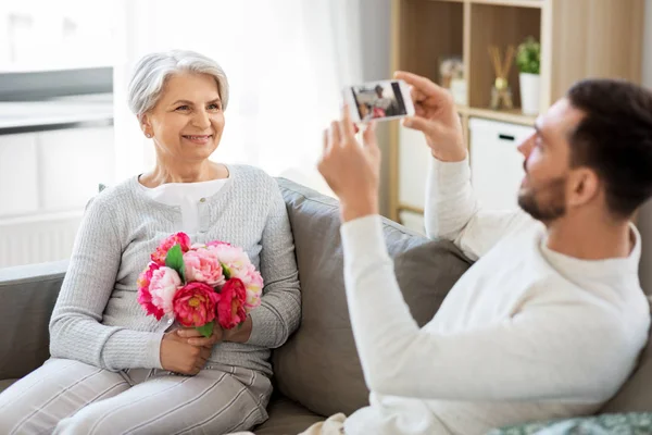 Yetişkin bir çocuk, yaşlı bir annenin fotoğrafını çekiyor. — Stok fotoğraf