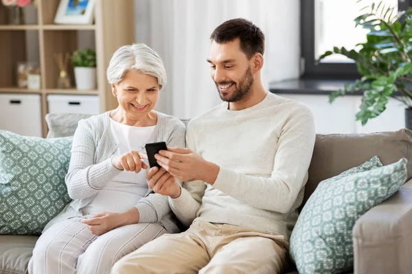 Oude moeder en volwassen zoon met smartphone thuis — Stockfoto