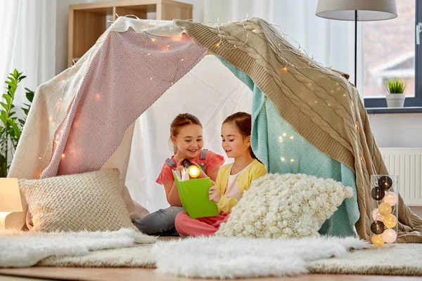 Happy girls reading book in kids tent at home — Stock Photo, Image