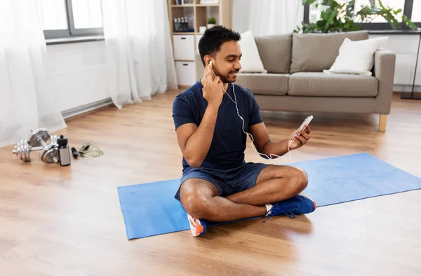 Hombre indio con teléfono inteligente en alfombra de ejercicio en casa —  Fotos de Stock