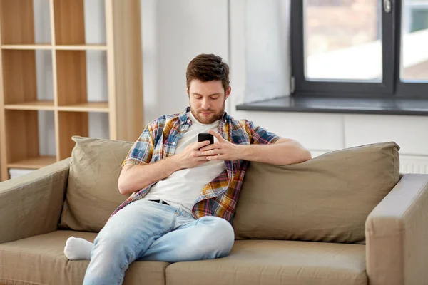 Hombre con teléfono inteligente sentado en el sofá en el nuevo hogar — Foto de Stock