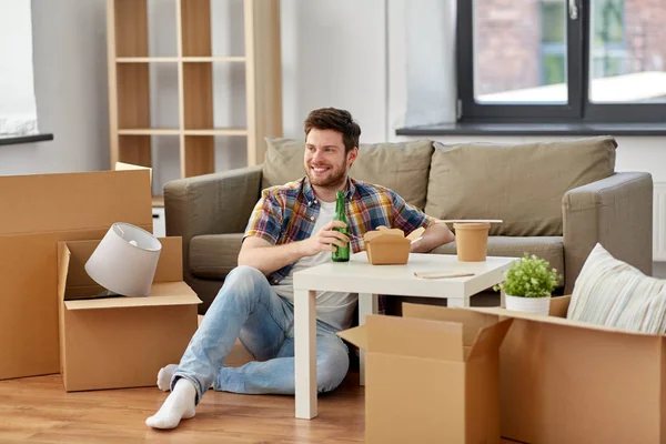 Hombre sonriente bebiendo cerveza y comiendo en casa nueva —  Fotos de Stock