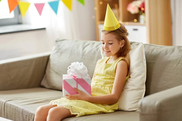 Chica feliz en sombrero de fiesta con regalo de cumpleaños en casa — Foto de Stock
