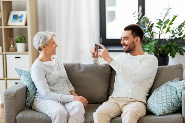 Hijo adulto fotografiando a la madre mayor en casa — Foto de Stock