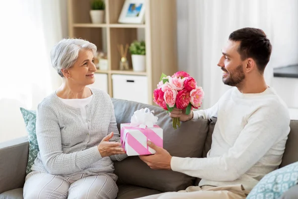 Son ge present och blommor till senior mor — Stockfoto