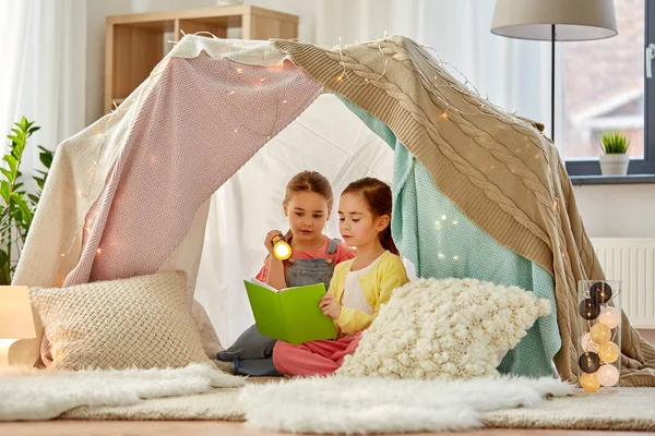 Happy girls reading book in kids tent at home — Stock Photo, Image