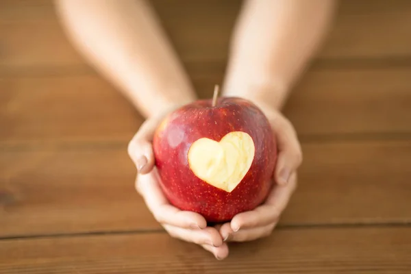 Zbliżenie rąk trzymając jabłko z rzeźbione serce — Zdjęcie stockowe