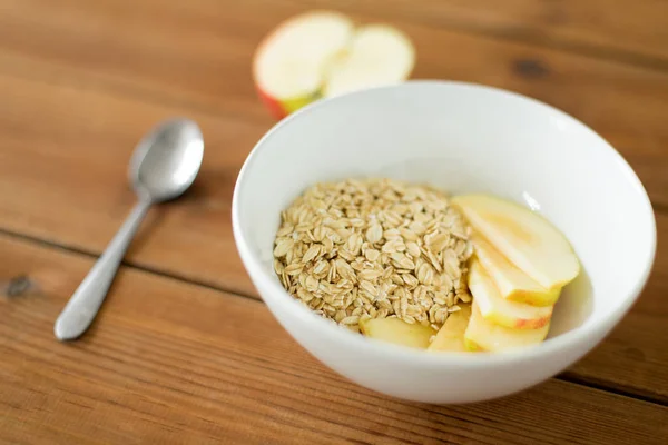 Oatmeal in bowl with apple and spoon on table — Stock Photo, Image