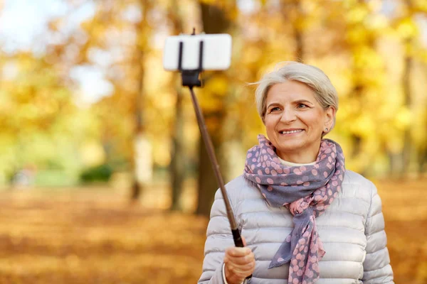 Starsza kobieta robi selfie w jesiennym parku — Zdjęcie stockowe
