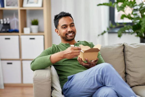 Hombre indio sonriente comiendo comida para llevar en casa — Foto de Stock