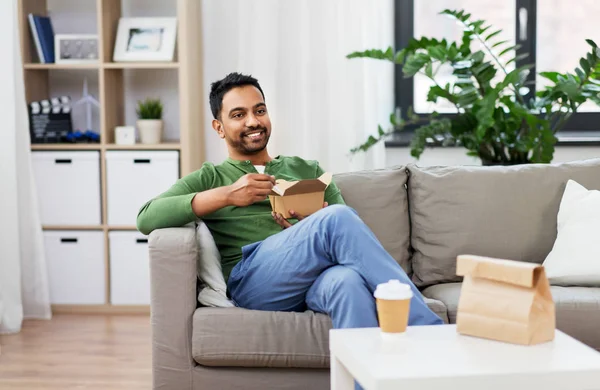 Hombre indio sonriente comiendo comida para llevar en casa — Foto de Stock