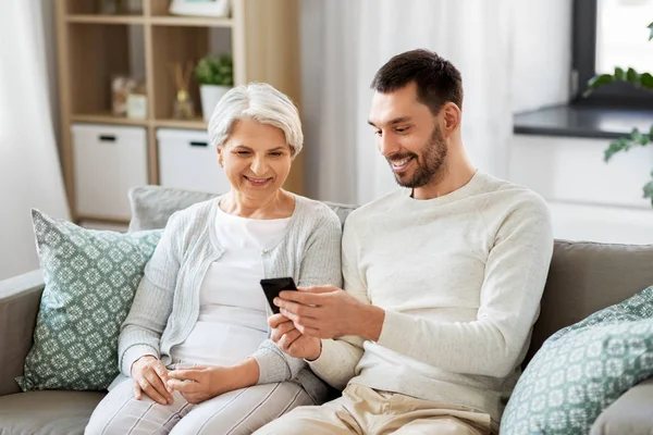 Mãe velha e filho adulto com smartphone em casa — Fotografia de Stock