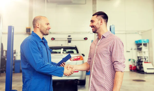 Auto mechanic and man shaking hands at car shop — Stock Photo, Image
