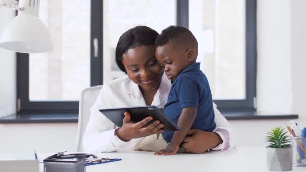 クリニックで赤ちゃんの患者にタブレットPCを示す医師 — ストック動画