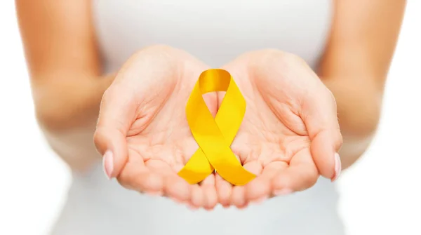 Mãos segurando fita consciência câncer ouro amarelo — Fotografia de Stock