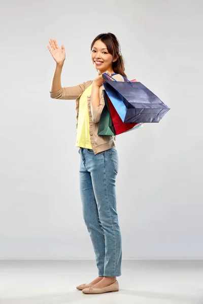 Χαρούμενη Ασιάτισσα με σακούλες να κουνάει το χέρι. — Φωτογραφία Αρχείου