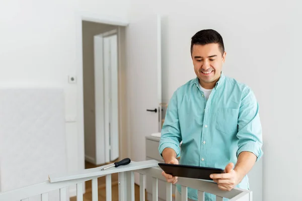 Padre con tablet pc assemblaggio lettino per bambini a casa — Foto Stock