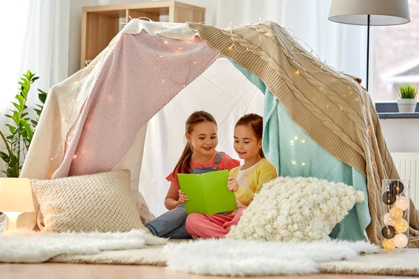 Happy girls reading book in kids tent at home — Stock Photo, Image