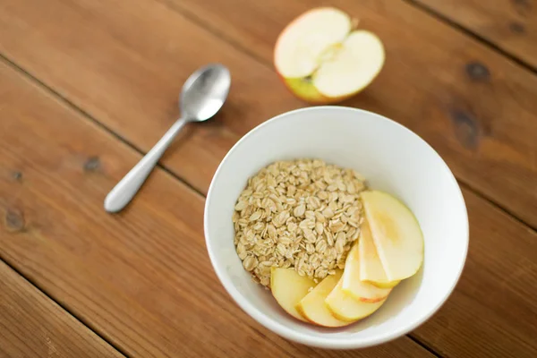 Oatmeal in bowl with apple and spoon on table — Stock Photo, Image