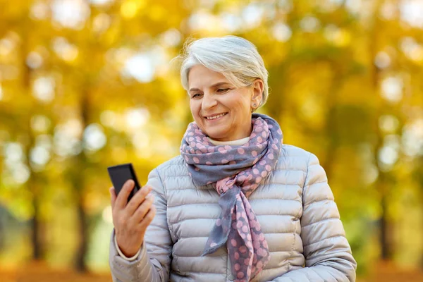 Mulher sênior feliz com smartphone no parque de outono — Fotografia de Stock