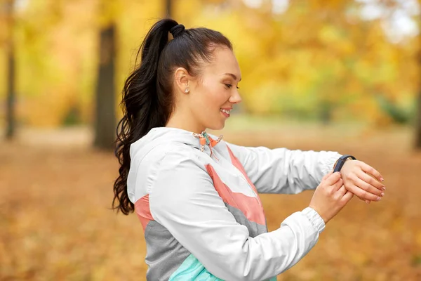 Женщина смотрит на фитнес-трекер в осеннем парке — стоковое фото
