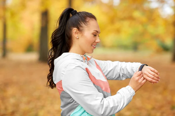 秋の公園でフィットネストラッカーを見ている女性は — ストック写真