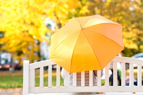 Donna con ombrellone seduta su panchina nel parco autunnale — Foto Stock