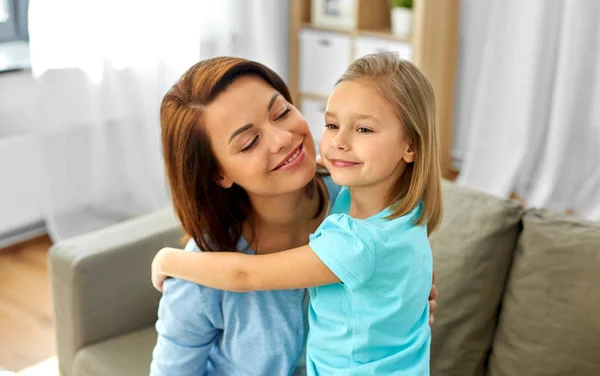 Pequena filha abraçando sua mãe em casa — Fotografia de Stock