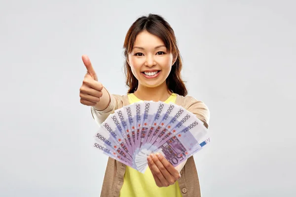 Avro parası olan Asyalı kadın başparmaklarını gösteriyor — Stok fotoğraf