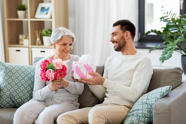 Hijo dando regalo y flores a la madre mayor — Foto de Stock