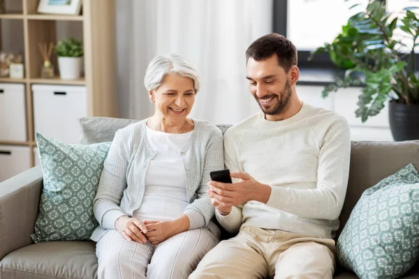 Alte Mutter und erwachsener Sohn mit Smartphone zu Hause — Stockfoto