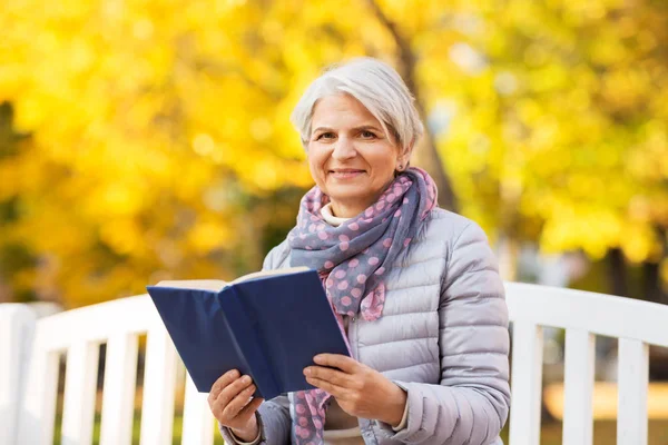 Gelukkig senior vrouw lezen boek in de herfst park — Stockfoto