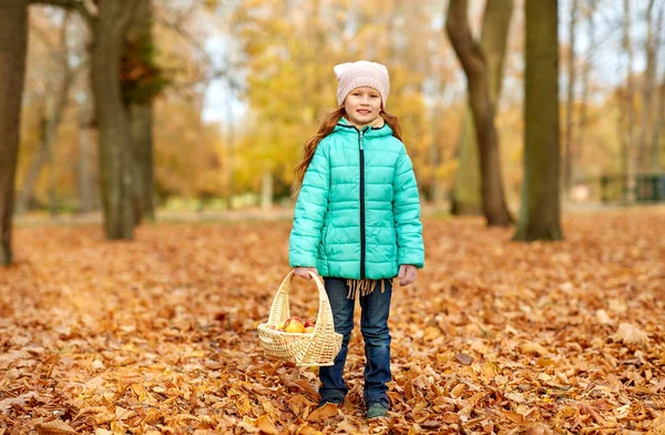 Девушка с яблоками в плетеной корзине в осеннем парке — стоковое фото