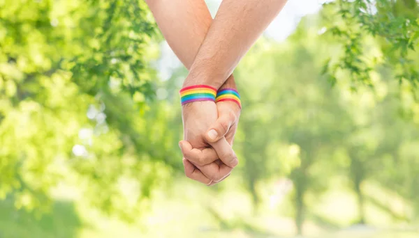 Mãos de casal com orgulho gay pulseiras arco-íris — Fotografia de Stock