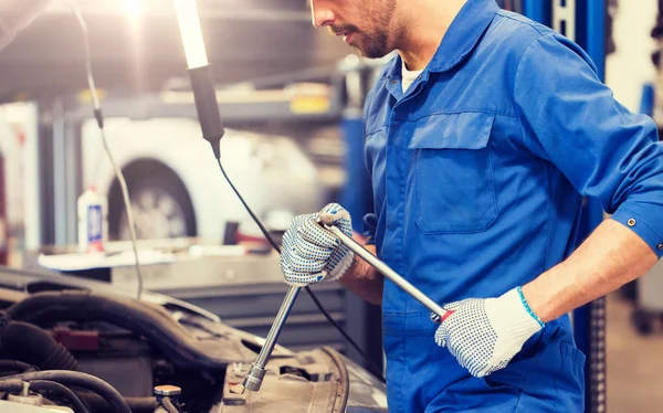 Mechanic man with wrench repairing car at workshop — Stock Photo, Image