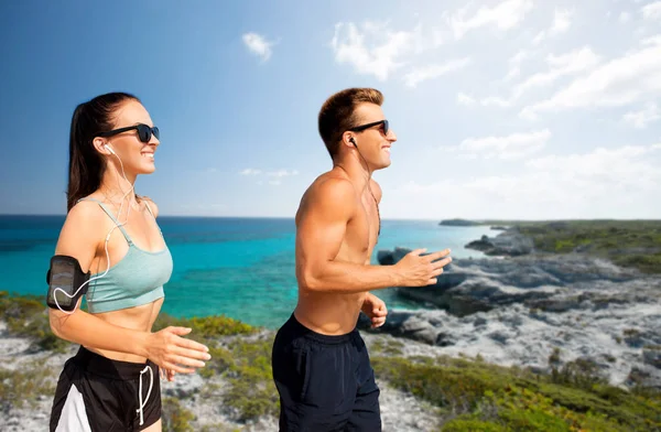 Par med telefoner och armband som löper på stranden — Stockfoto