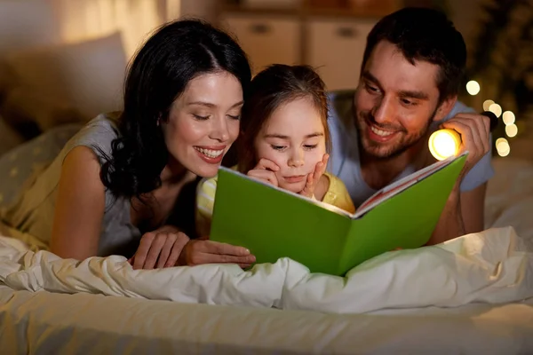 Happy family reading book in bed at night at home — Stock Photo, Image
