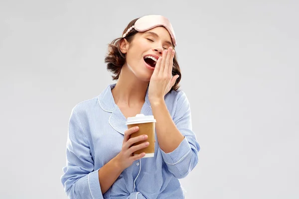 Woman in pajama and eye mask with coffee yawning — Stock Photo, Image