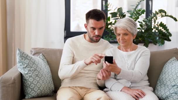 Madre anciana e hijo adulto con teléfono inteligente en casa — Vídeos de Stock