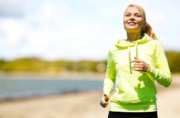 Donna sorridente che corre lungo la spiaggia — Foto Stock