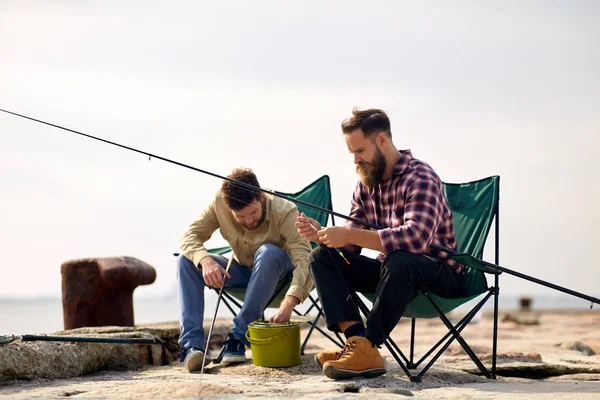 Friends adjusting fishing rods with bait on pier Stock Image