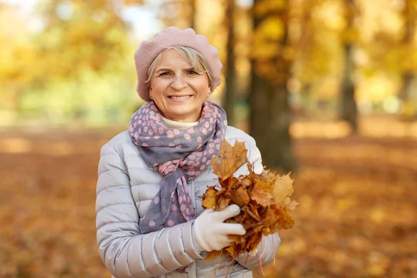 Mulher sênior com folhas de bordo no parque de outono — Fotografia de Stock
