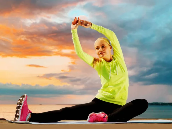 Kvinna stretching på träningsmatta vid havet — Stockfoto