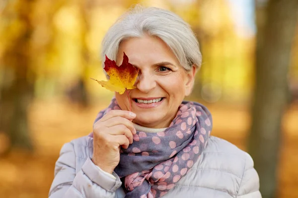 Mulher sênior feliz com folha de bordo no parque de outono — Fotografia de Stock