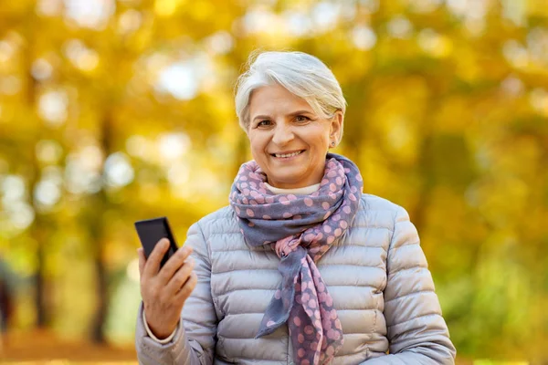 Felice donna anziana con smartphone al parco autunnale Foto Stock