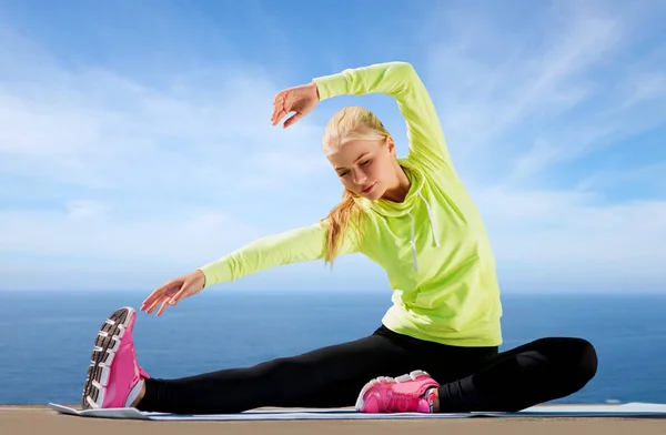 Vrouw stretching op oefening mat over zee — Stockfoto