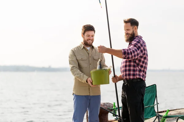 Amis masculins avec des poissons et des cannes à pêche sur jetée Images De Stock Libres De Droits