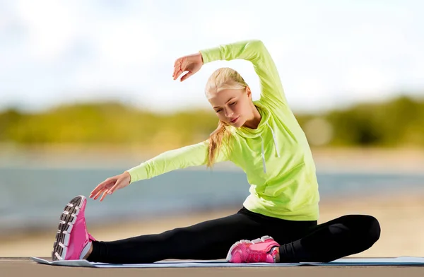 Женщина растягивается на тренировочном коврике на пляже — стоковое фото
